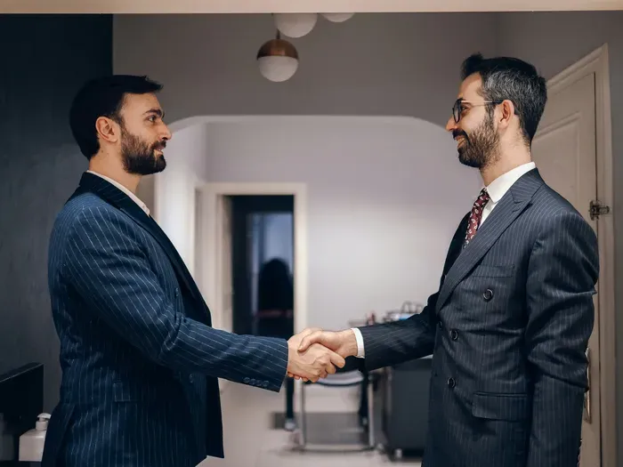 Two businessmen in suits shaking hands in modern office environment symbolizing successful partnership for Town Service Online